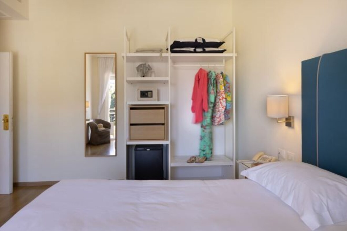 Une chambre d’hôtel comprenant un lit, une armoire, un miroir, un bureau avec une lampe et un téléphone.