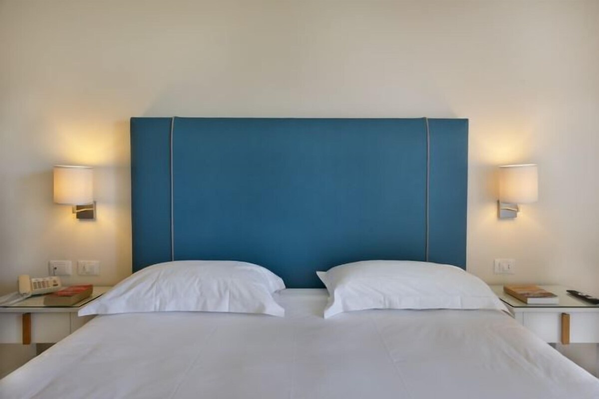 A hotel room with a large bed, two bedside tables, and wall-mounted lamps.