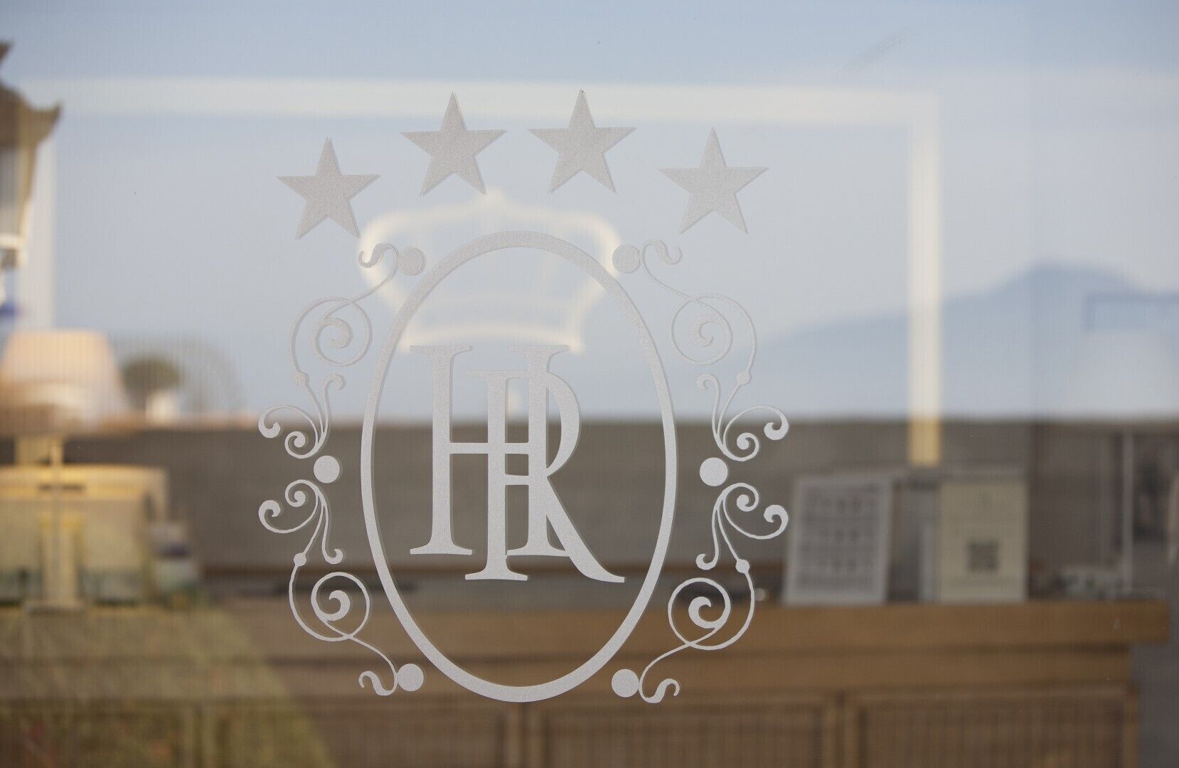 Une fenêtre ornée d’un motif décoratif représentant les lettres « HR » et des étoiles, avec un arrière-plan flou de bâtiments.