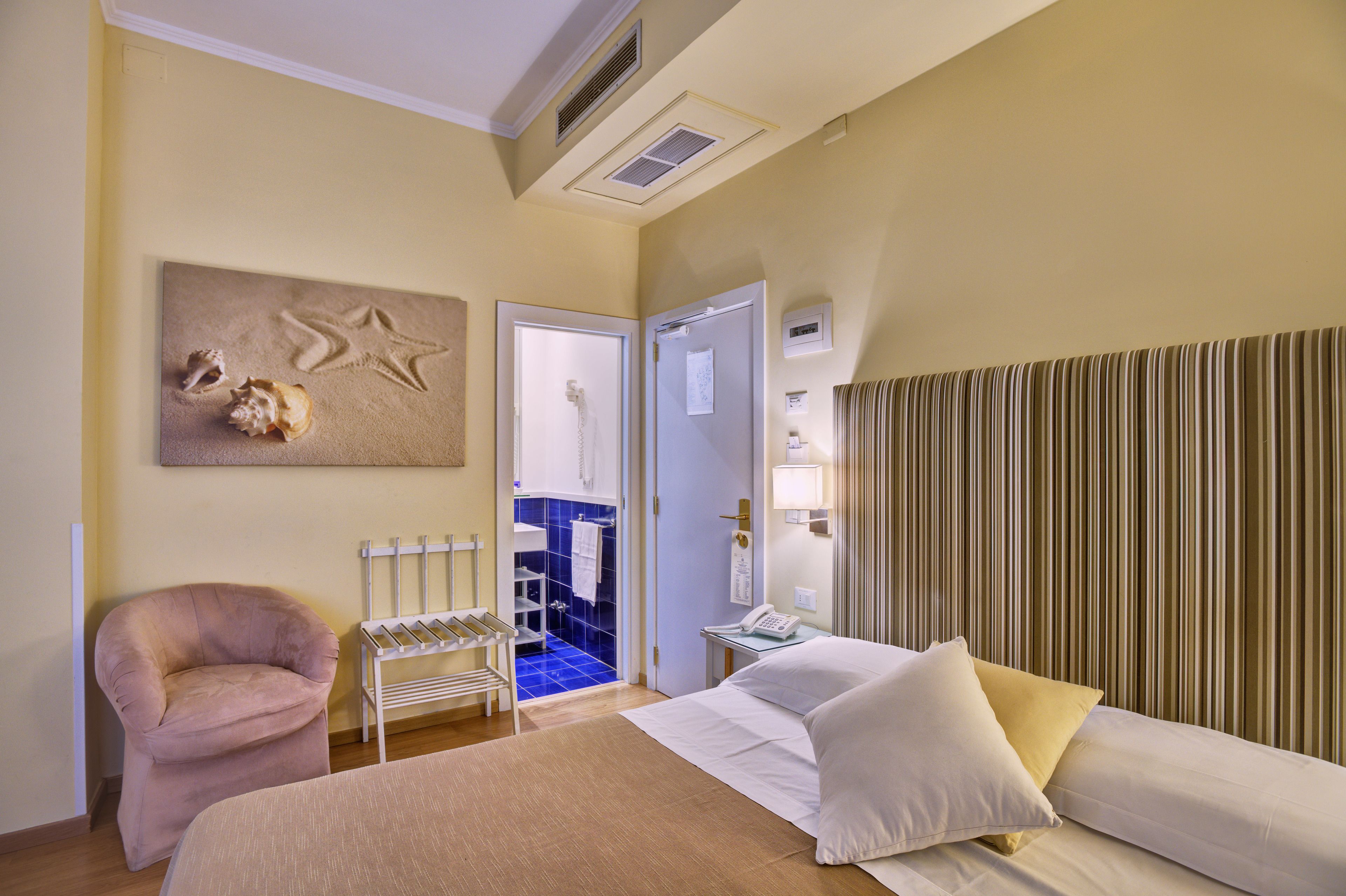 A hotel room with a bed, a chair, a desk, and a bathroom visible through an open door.