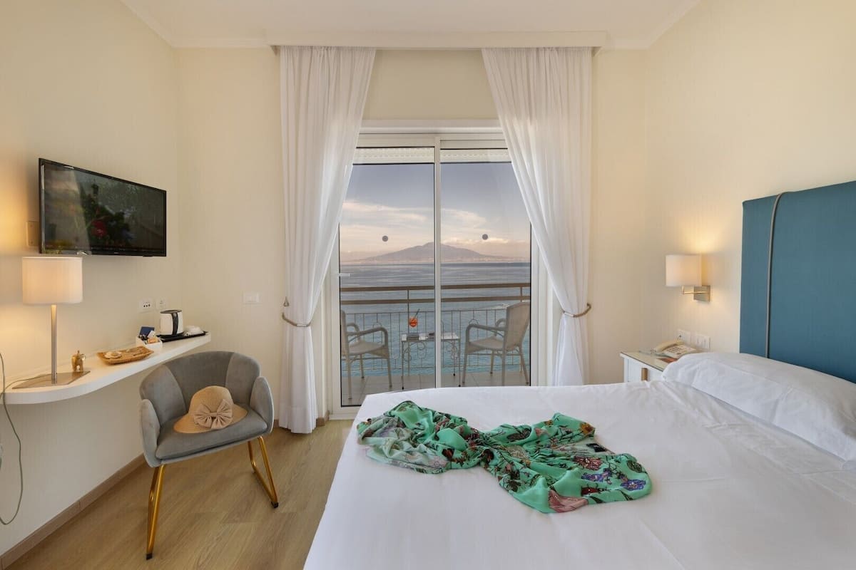 Een hotelkamer met een bed, een stoel, een televisie, een balkon met uitzicht en een telefoon.