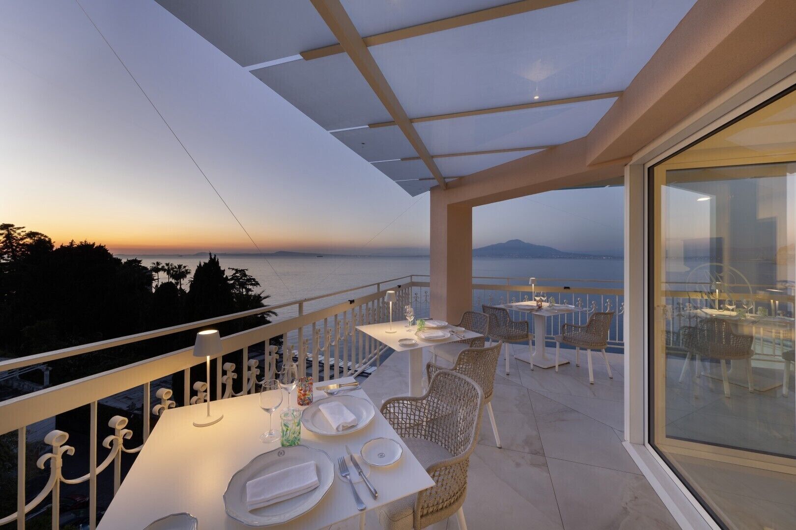 A terrace with tables set for dining, overlooking a body of water and distant land.