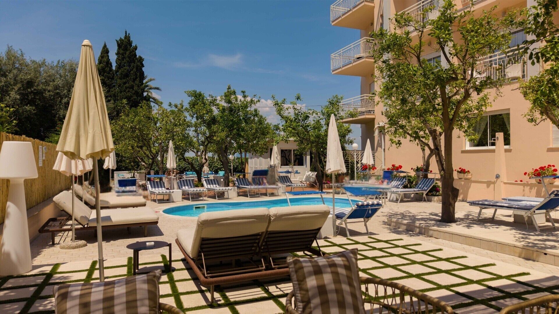 Zona junto a la piscina con sillas de descanso, sombrillas y un edificio al fondo.