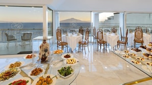 Ein Essbereich mit Tischen und Stühlen, ein Buffet mit verschiedenen Speisen und Blick auf das Meer.
