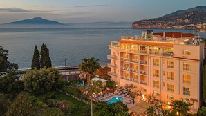 Ein Hotel mit Pool, mehreren Balkonen und Blick auf das Meer und die Berge.