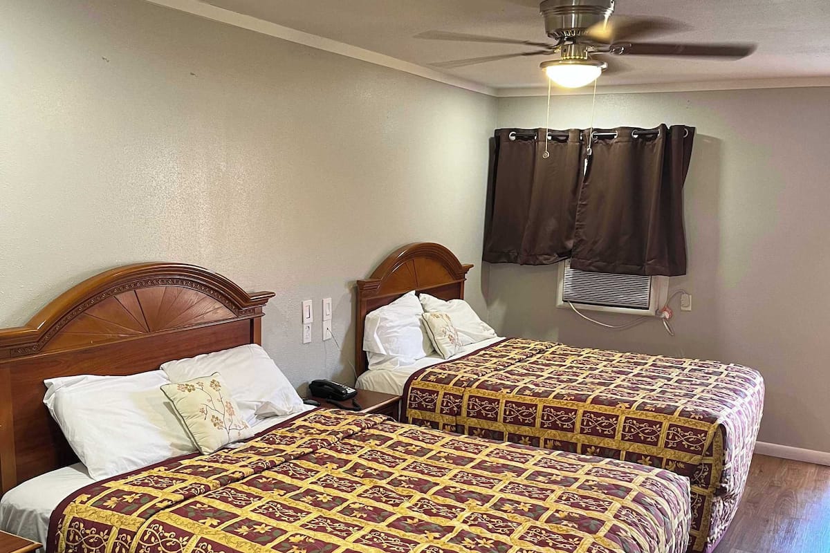 A hotel room with two beds, wooden headboards, a ceiling fan, and a window with curtains.