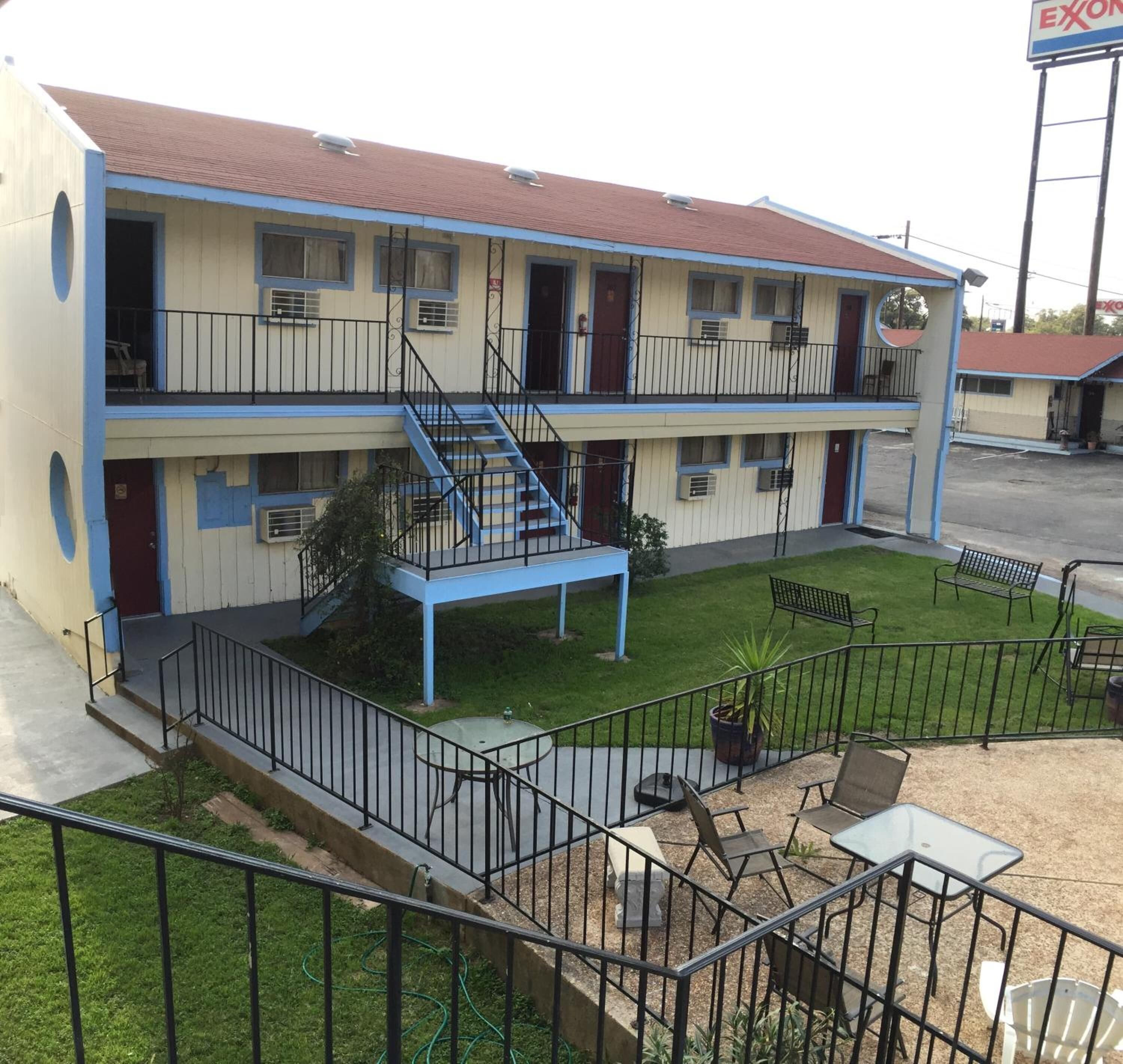 Un motel de dos plantas con una escalera central, asientos exteriores y un patio amurallado.