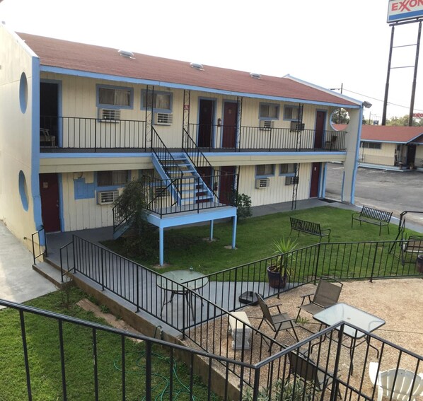 Um motel de dois andares com uma escadaria central, área de estar externa e um pátio cercado.