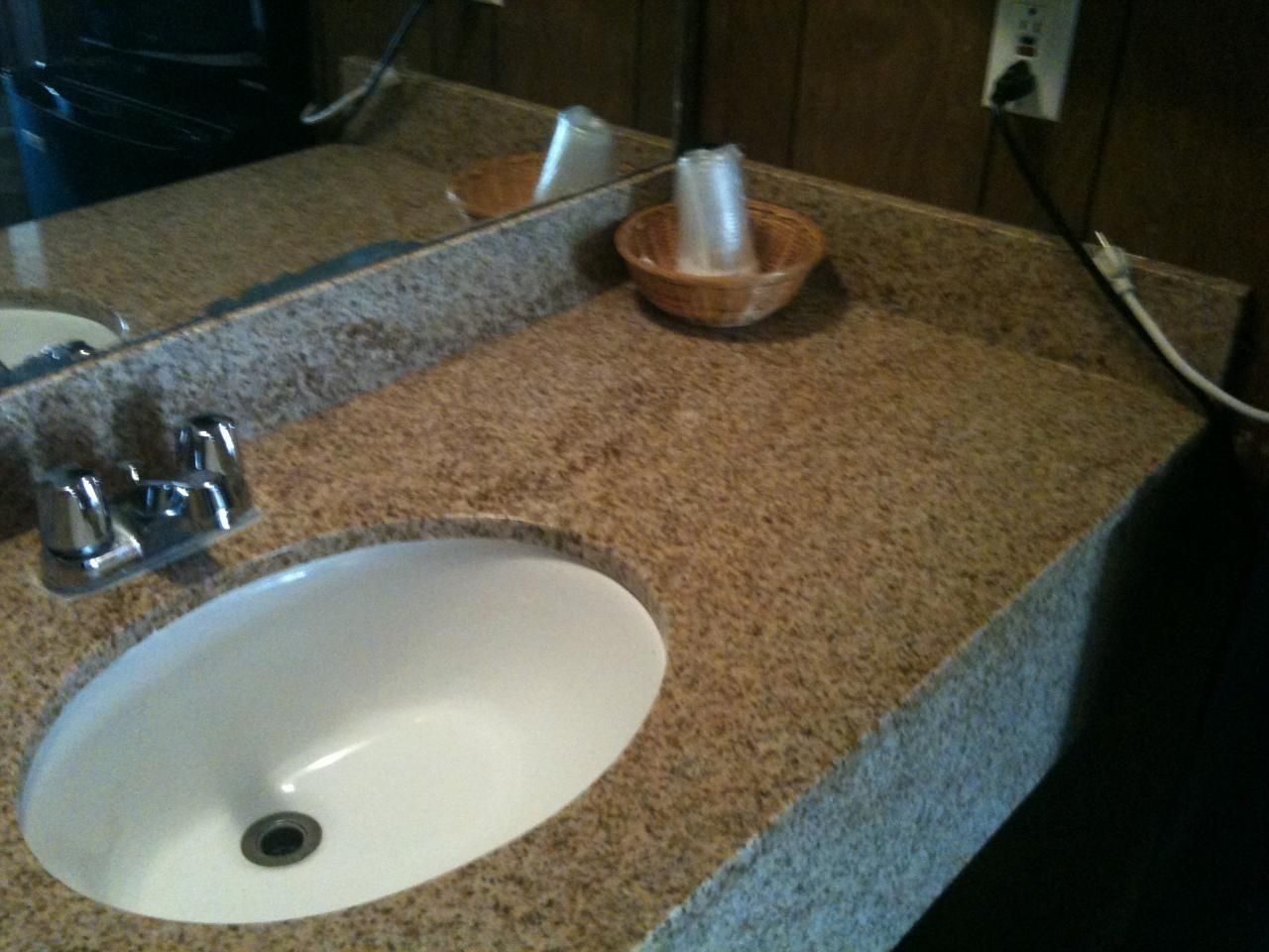 A bathroom with a granite countertop, a white sink, a mirror, and a soap dish.