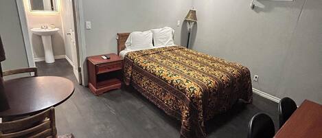 Een slaapkamer met een bed, nachtkastje, lamp en een kleine tafel met stoelen.