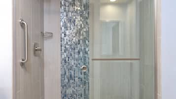 A modern shower with a glass door, a handrail, and a tiled wall.