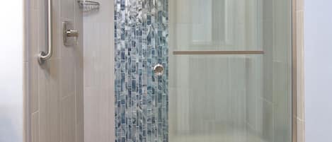 A modern shower with a glass door, a handrail, and a tiled wall.