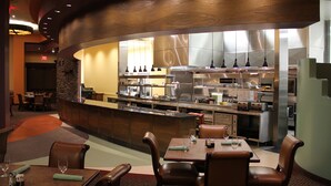 A restaurant with a curved counter, leather chairs, and a visible kitchen area with stainless steel appliances.