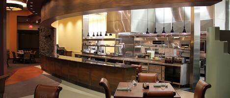 Un restaurante con una barra curva, sillas de cuero y una cocina visible con electrodomésticos de acero inoxidable.