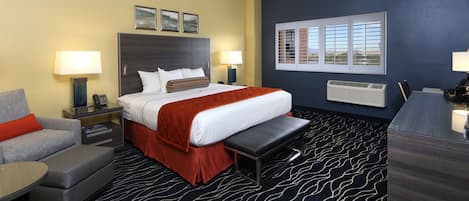 Une chambre d’hôtel comprenant un lit, des tables de chevet, un bureau, une chaise, un banc et une fenêtre.