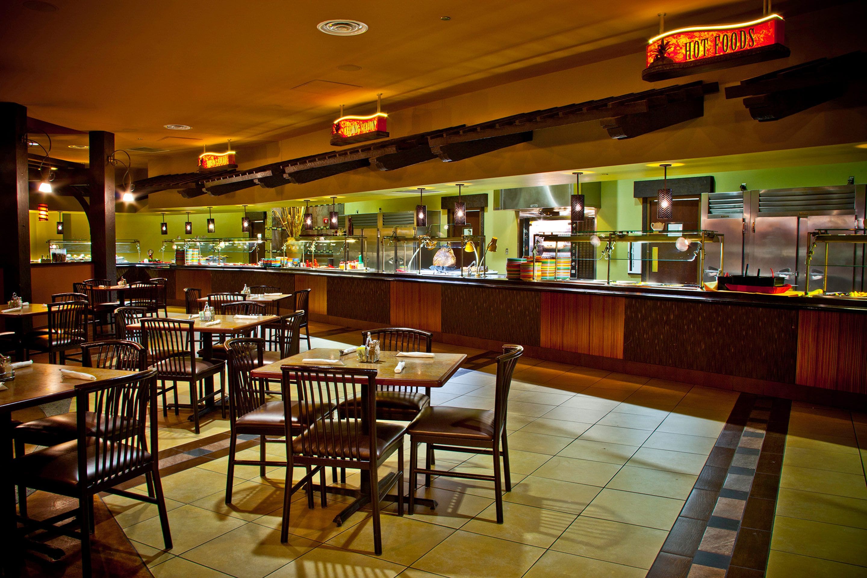 A restaurant with multiple tables and chairs, a counter with food display, and a sign indicating 'HOT FOODS'.