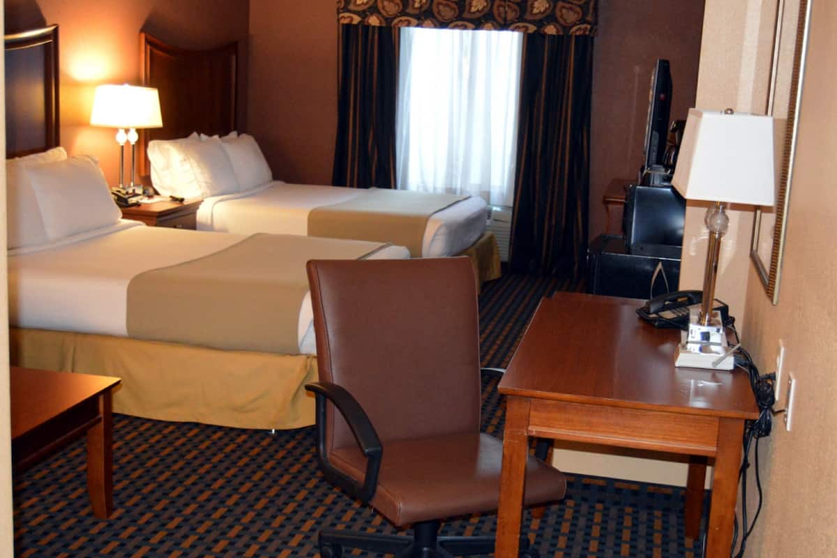 A hotel room with two beds, a desk, a chair, a TV, and a lamp.