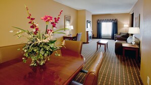 A hotel room with a dining table, chairs, a sofa, a TV, and a fireplace.