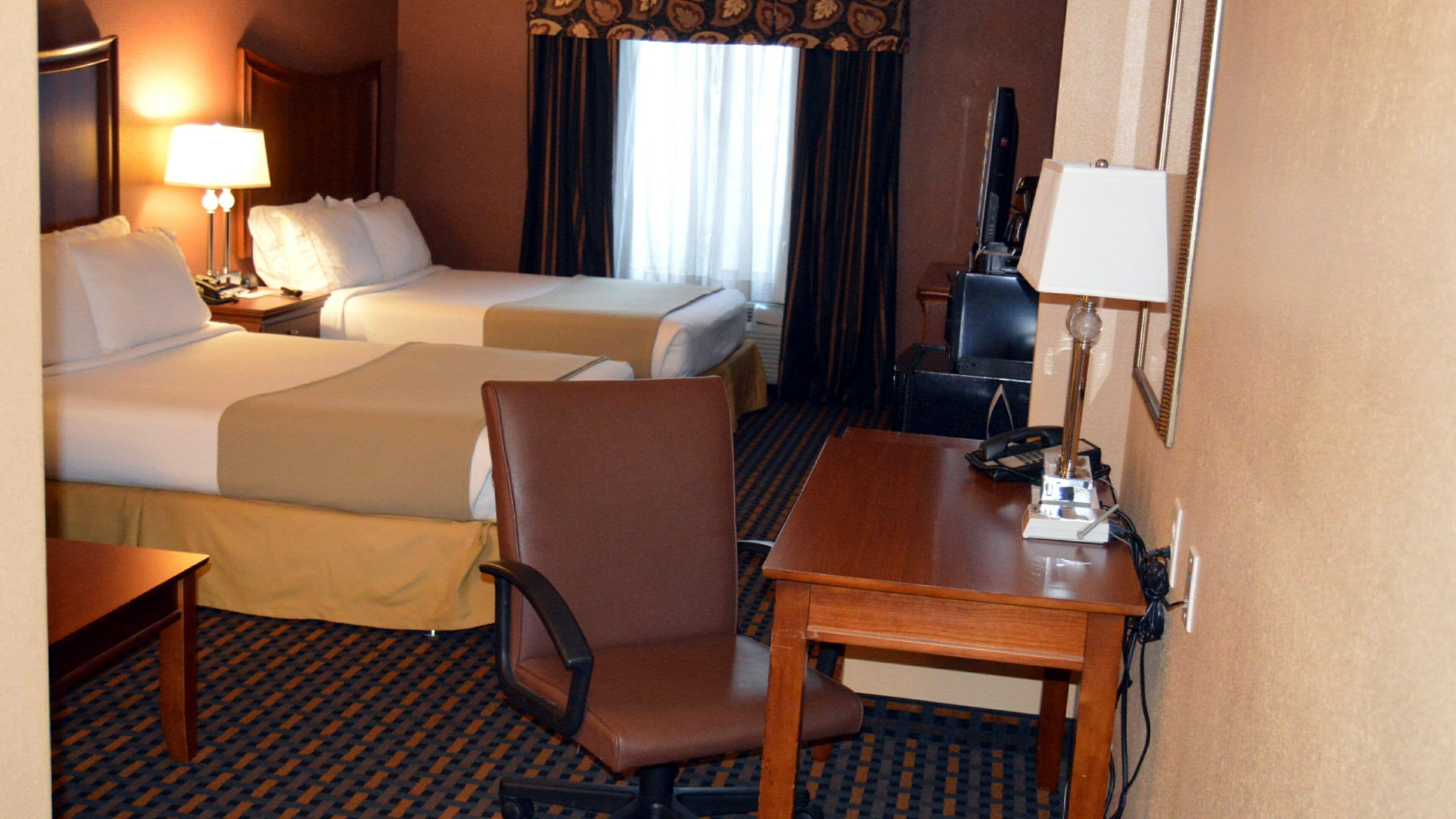 Une chambre d’hôtel avec deux lits, un bureau, une chaise, une télévision et une lampe.