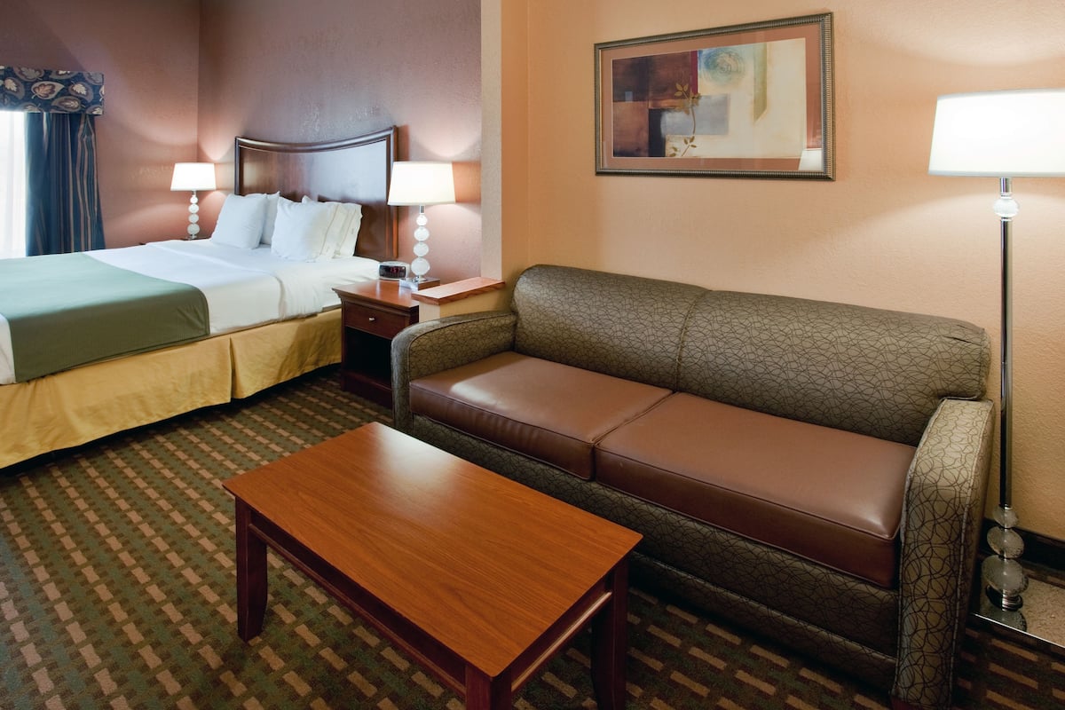 A hotel room with a bed, a sofa, a table, and a lamp.