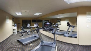 Une salle de remise en forme équipée de tapis de course, d’un mur avec des miroirs et d’un petit bureau avec un ordinateur.