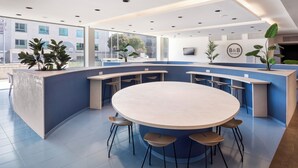 A modern hotel reception area with a curved counter, round table, and several bar stools. - B&B Madrid Aeropuerto T1 T2 T3 (Madrid)
