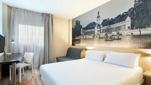 A hotel room with a large bed, a desk, a chair, and a wall-mounted TV. - B&B Madrid Aeropuerto T1 T2 T3 (Madrid)