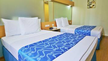 Habitación de hotel con dos camas, cada una con sábanas blancas y una colcha de diseño azul. Se aprecia un cabecero de madera, una mesita de noche con un teléfono y un espejo montado en la pared.