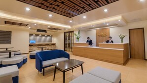A hotel reception area with a wooden reception desk, blue and grey seating, and a kitchenette in the background. - Microtel by Wyndham Davao (Davao)