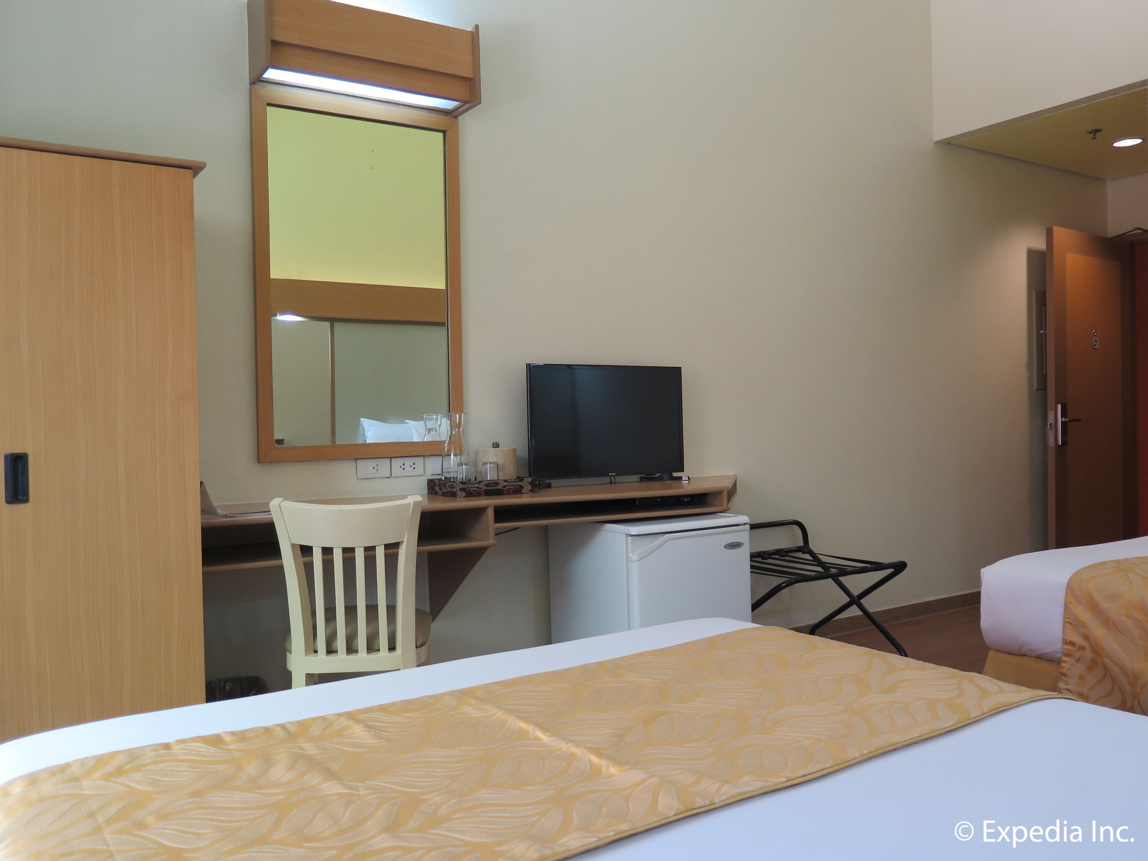 A hotel room with a bed, a desk with a television, a chair, and a wardrobe.