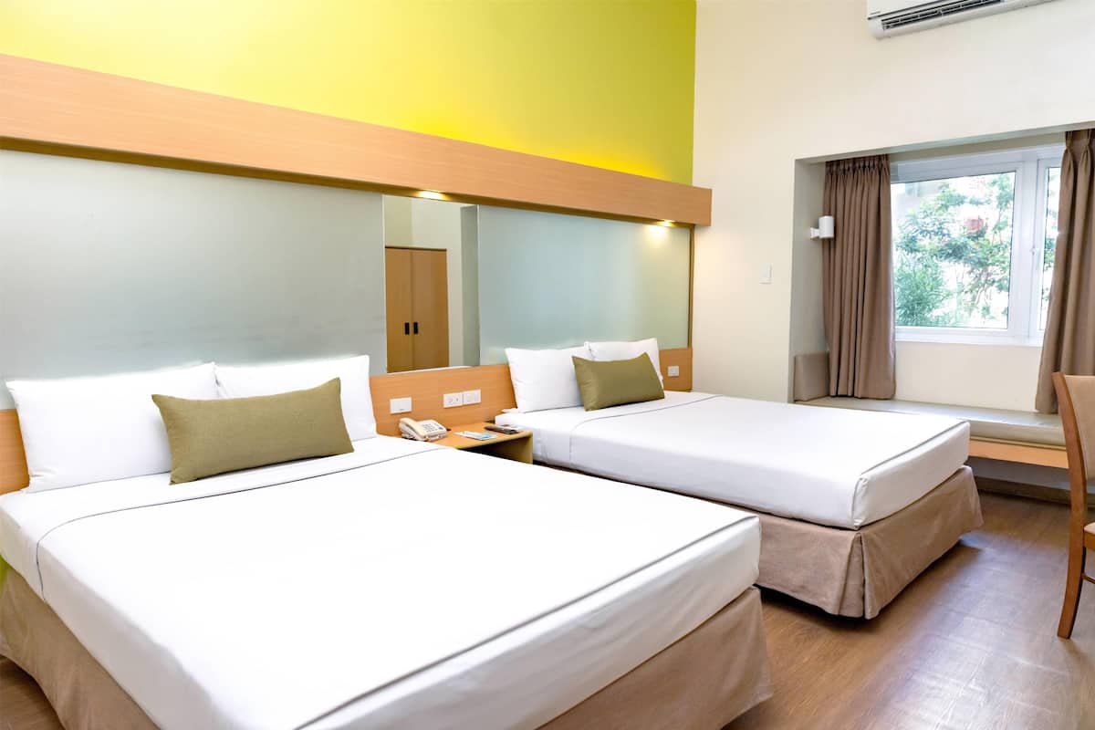 A hotel room with two beds, a mirror, a bedside table with a phone, and a window with curtains.