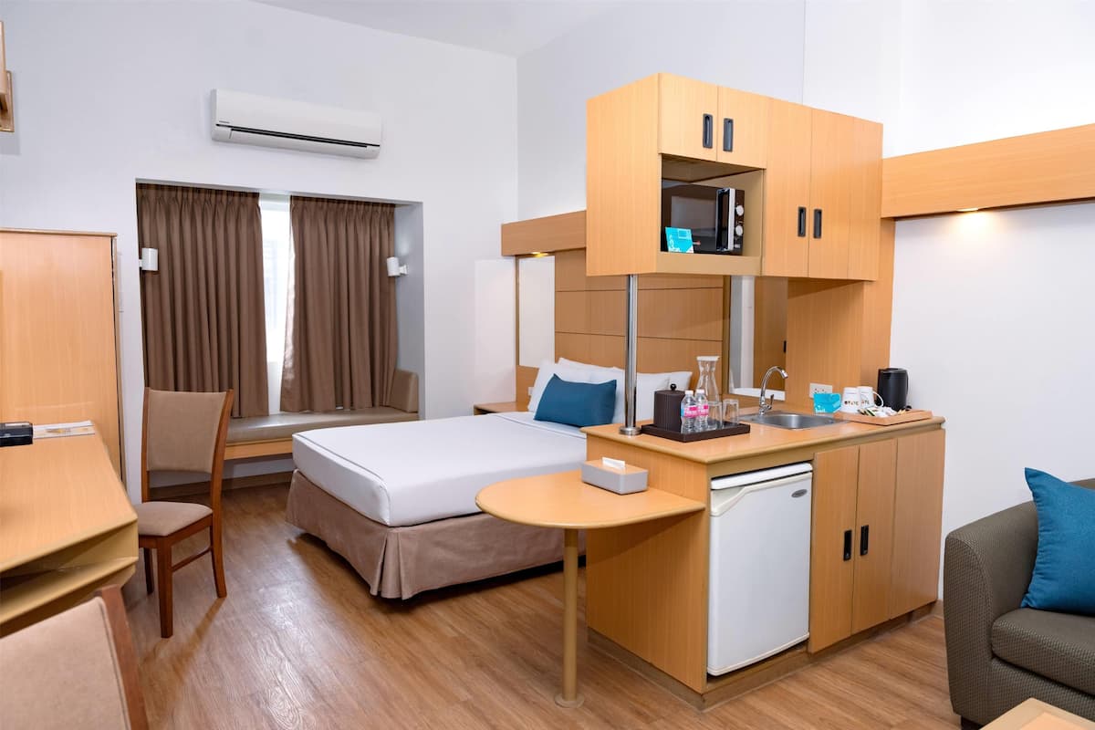 A compact hotel room with a bed, a desk, a chair, a small kitchenette, and a sofa.
