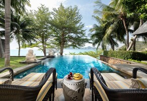 Zona junto a la piscina con sillas de mimbre, una urna decorativa y vista al mar.