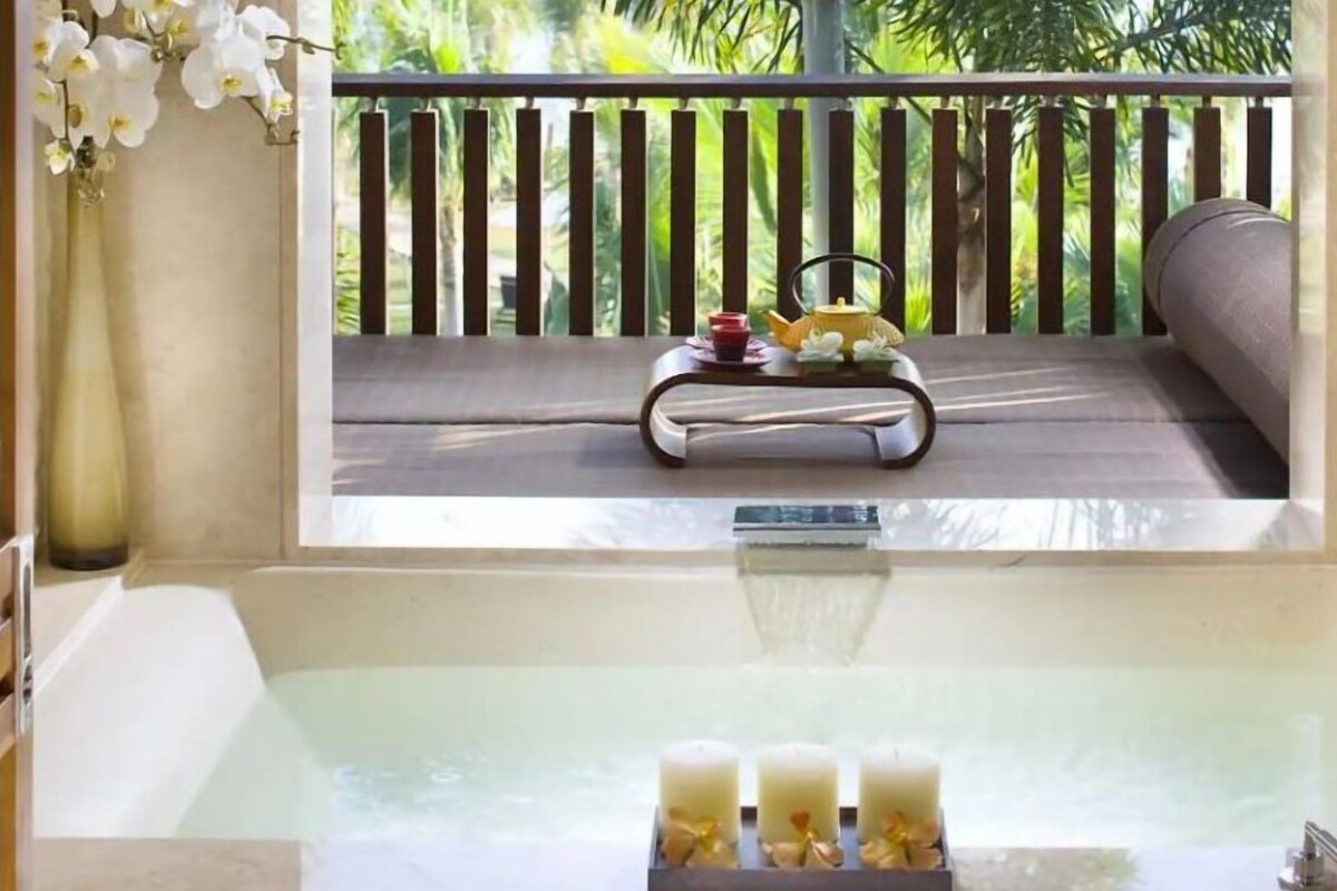A bathtub with a view of a balcony, a vase with flowers, and a tray with tea and a teapot.