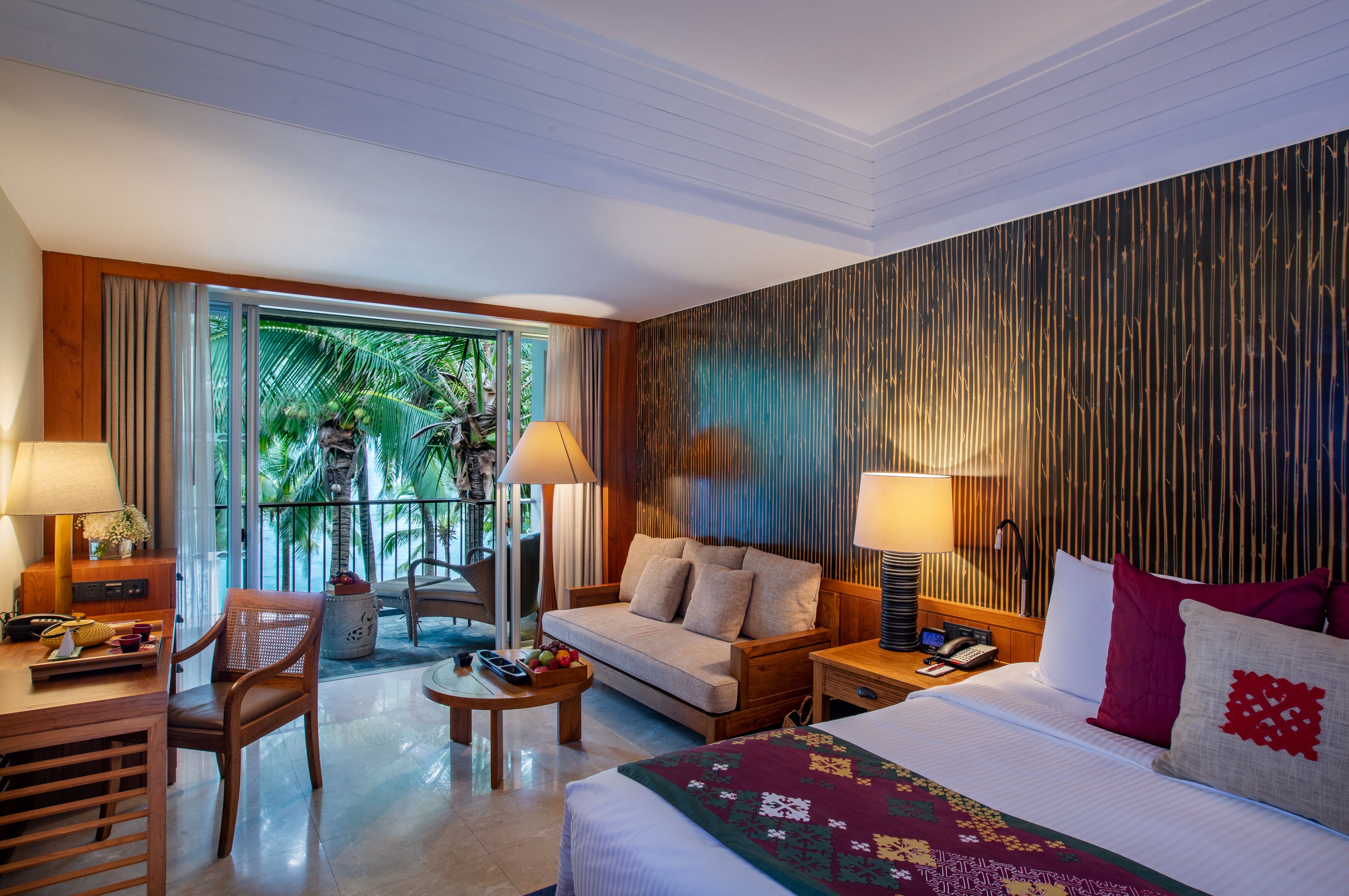 Habitación de hotel con sofá, cama, escritorio y silla. Ventana con cortinas y vistas a palmeras.