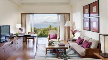 A spacious living room with a large TV, a sofa, a coffee table, and a dining area with a view of the ocean.