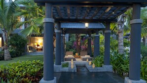 Un espacio exterior cubierto con pilares de piedra, una fuente de agua y asientos bajo una pérgola.