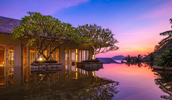 A serene resort setting with a reflective pool, a well-lit building with glass doors, and a sunset view. - Mandarin Oriental, Sanya (Sanya)