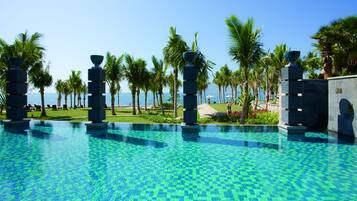 A pool with a tiled pattern, palm trees, and a view of the ocean.