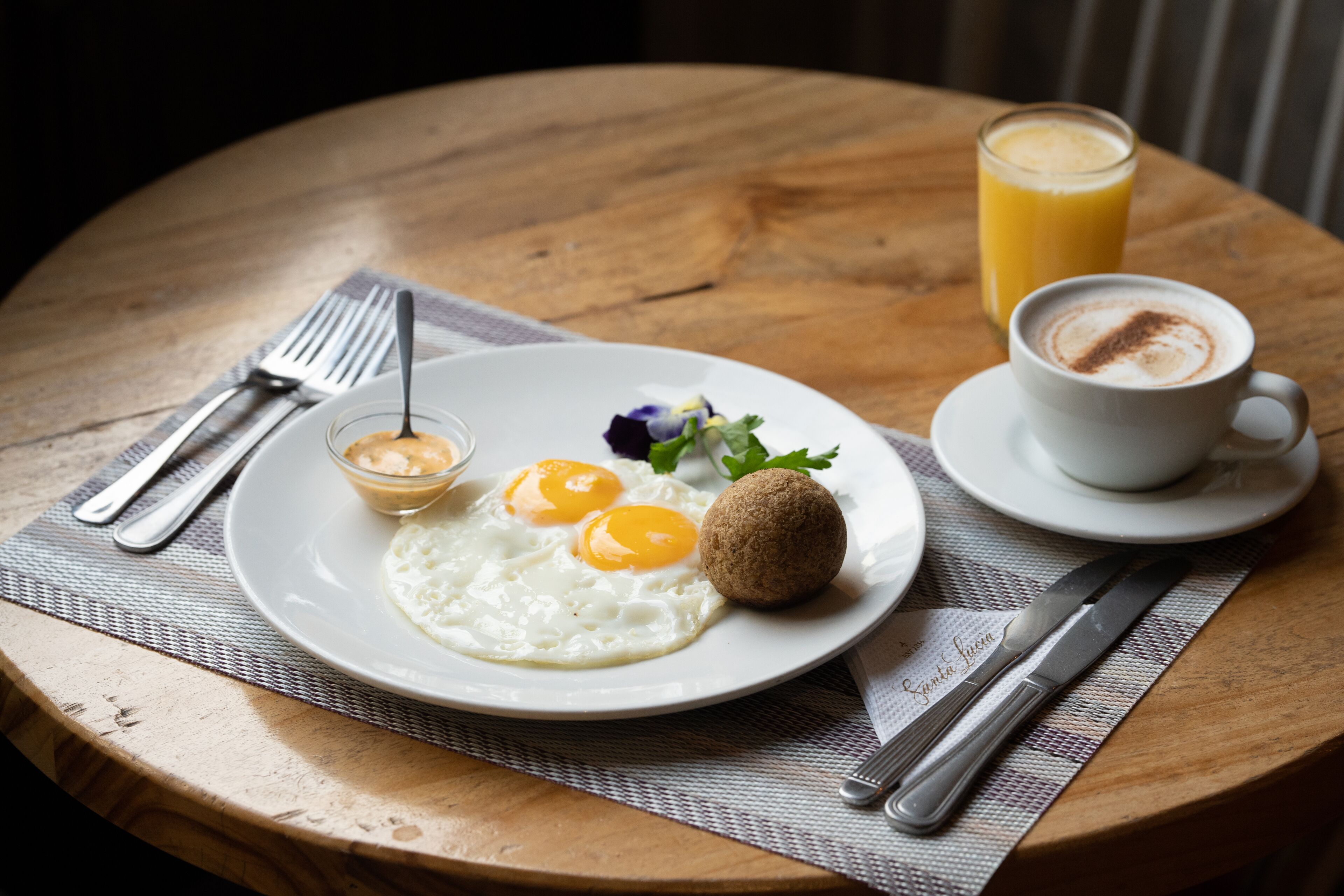 Une table en bois dressée pour le petit-déjeuner, avec des œufs, un muffin, un verre de jus d’orange et une tasse de café.