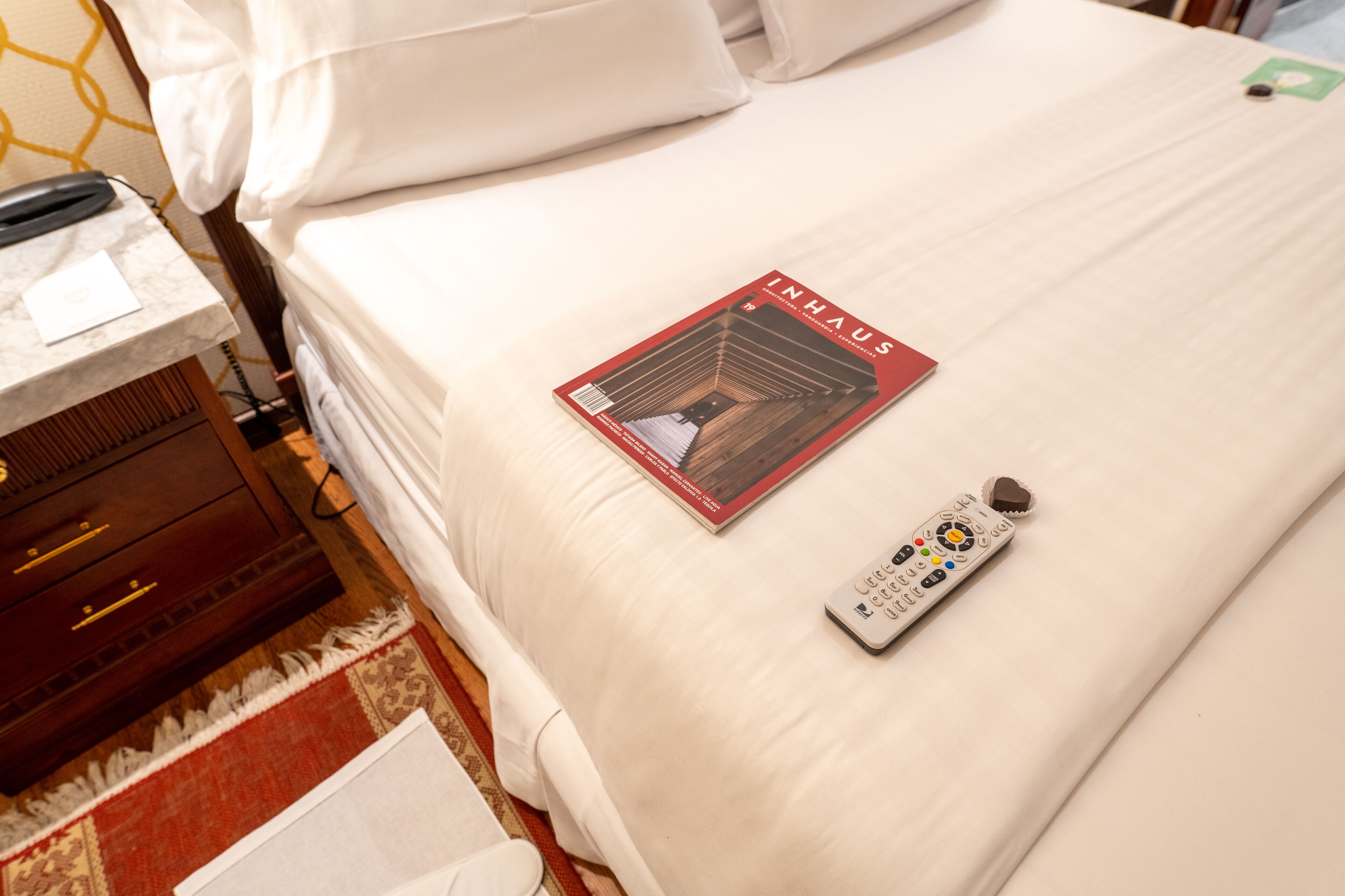 Habitación de hotel con una cama bien hecha, un control remoto y una revista sobre la cama.