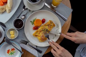 Desayuno con un plato de comida que incluye una porción de tortilla, tomates y una ramita de hierbas.