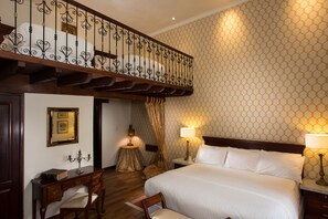 A hotel room with a large bed, two bedside tables with lamps, a wooden desk with a chair, a small round table with a lamp, and a decorative mirror on the wall. - Hotel Boutique Santa Lucia (Cuenca)