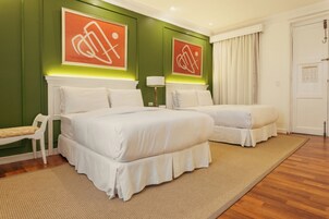 Habitación de hotel con dos camas, un banco y obras de arte en las paredes.