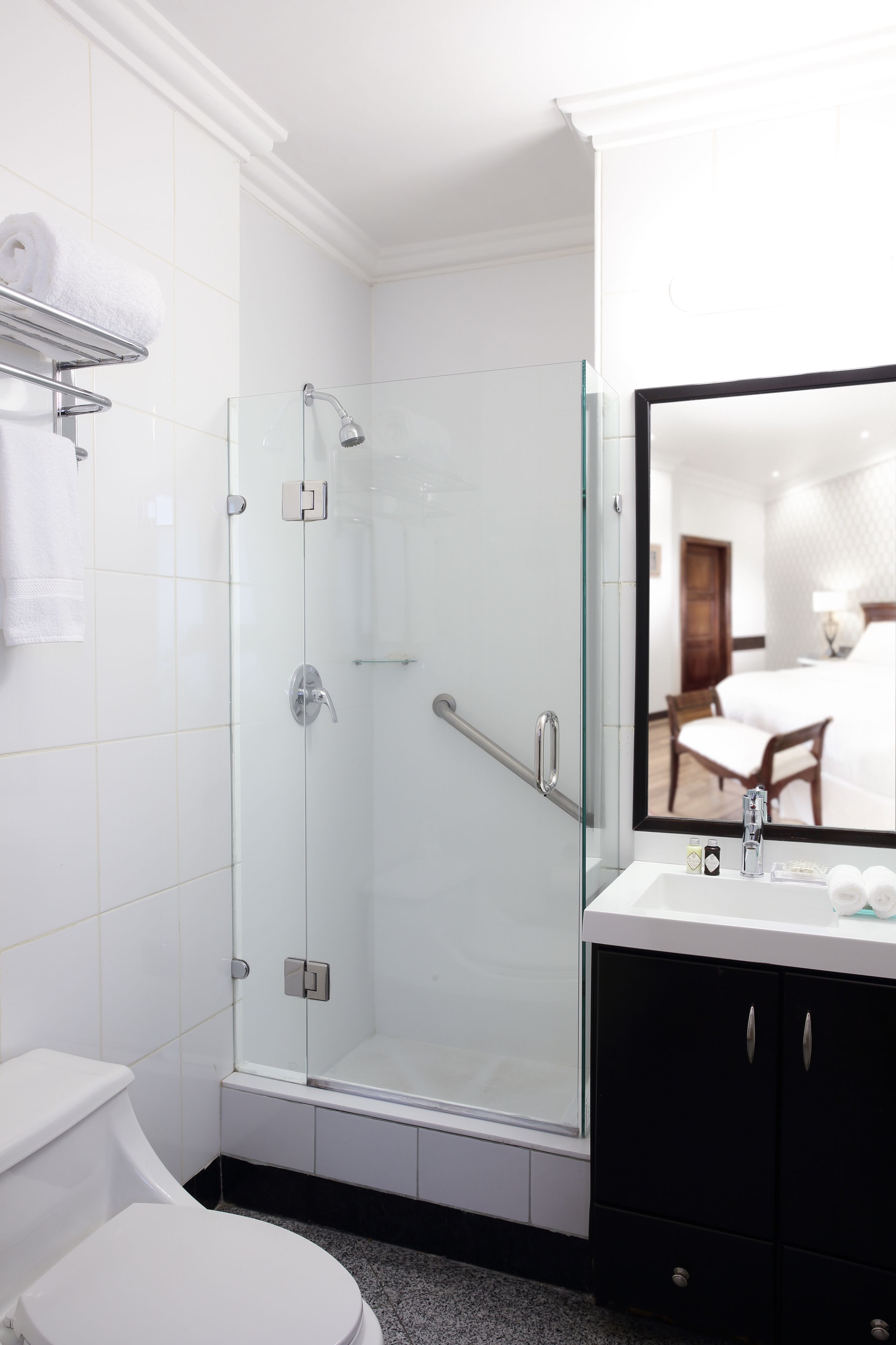 A modern bathroom with a glass-enclosed shower, a white toilet, a black vanity with a mirror, and a towel rack with folded towels.