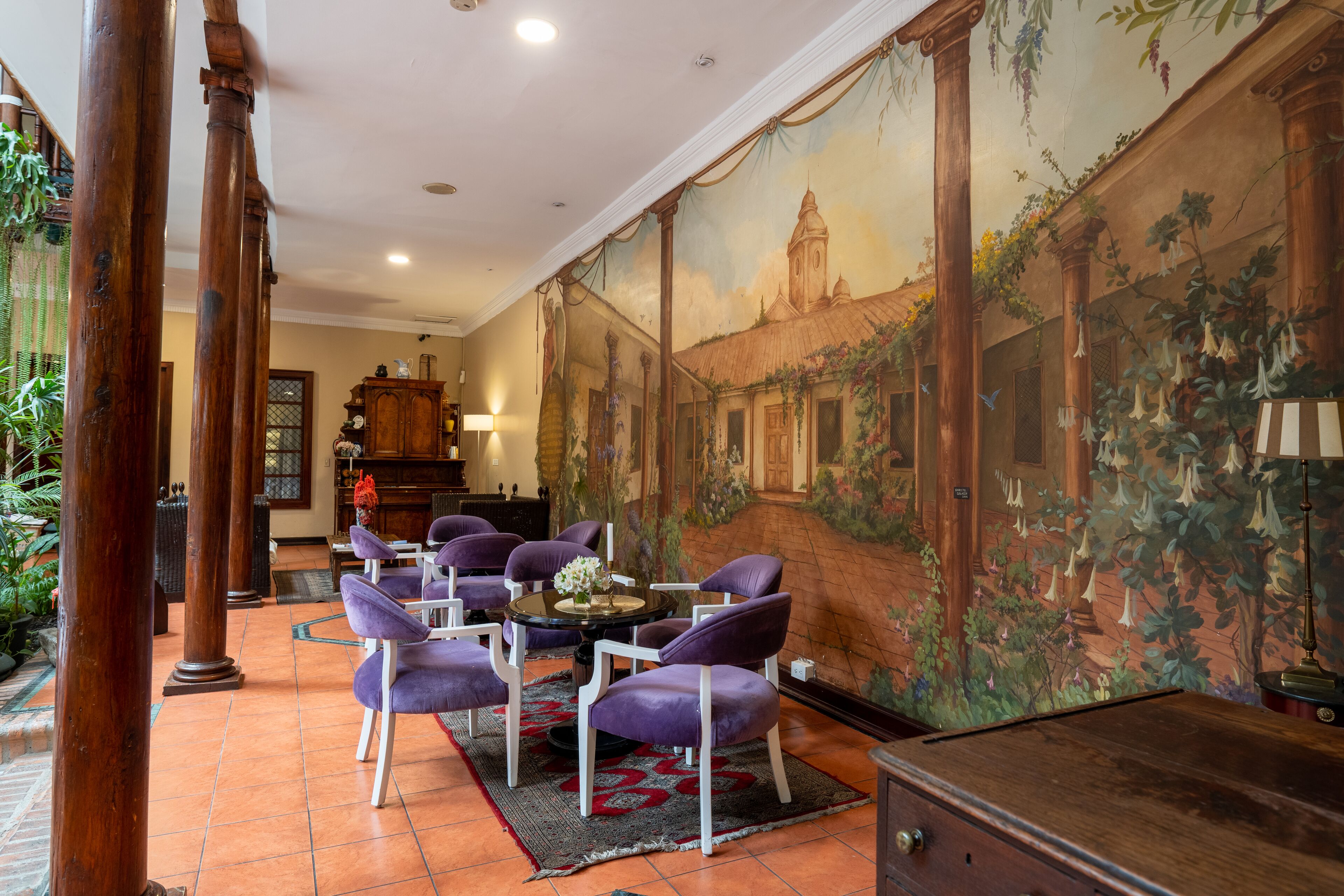A room with a mural, a dining area with purple chairs, and a wooden cabinet.