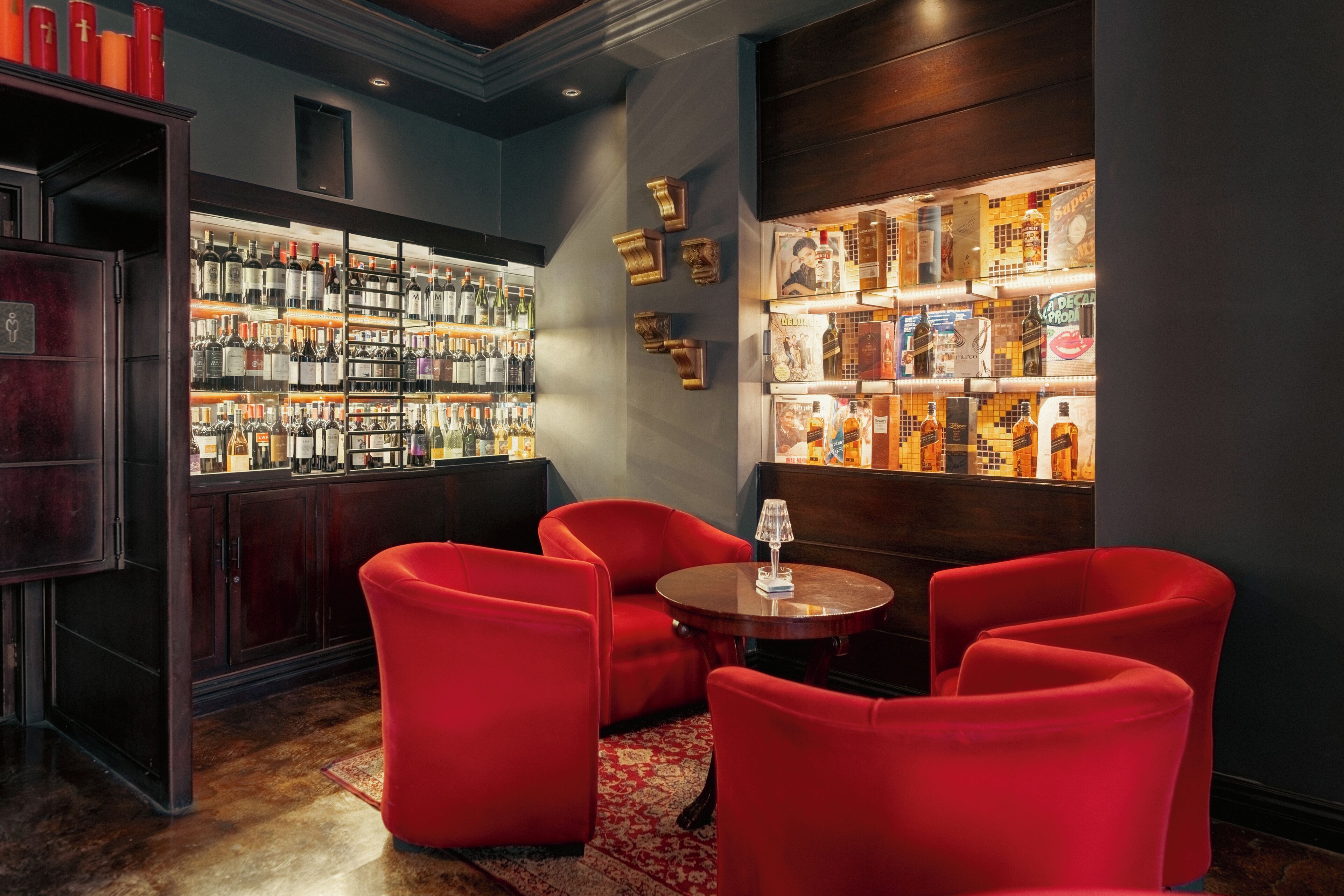 Un coin bar avec des chaises rouges, une table ronde et des étagères remplies de bouteilles d’alcool.