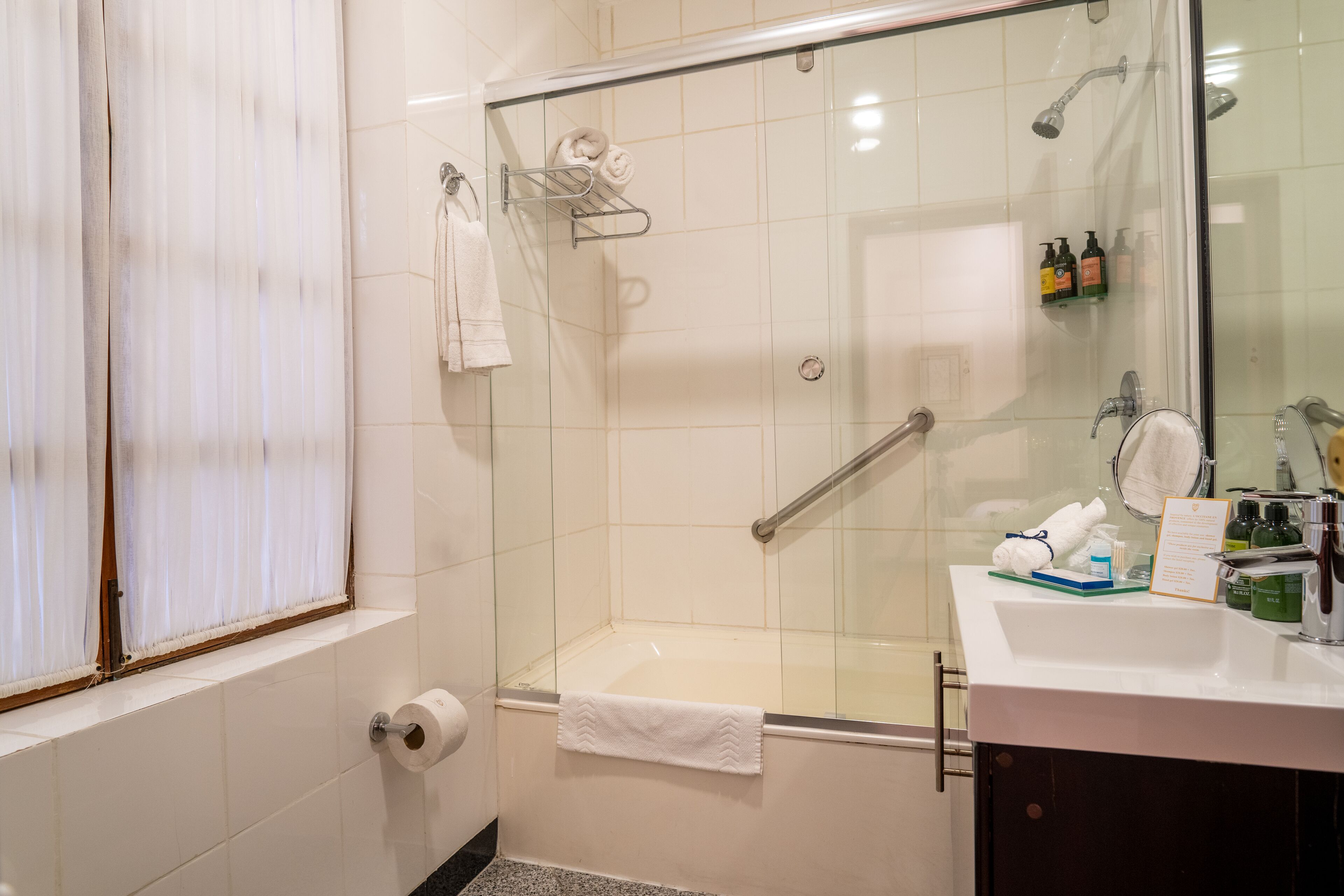 Un baño moderno con ducha envuelta en vidrio, un lavabo blanco con artículos de aseo y un perchero para toallas.