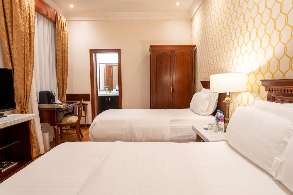 A hotel room with two beds, a desk with a computer, a wardrobe, and a lamp.