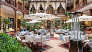 Un vaste espace de restauration intérieur, doté de nombreuses tables et chaises, agrémenté de plantes en pot et comprenant une fontaine décorative centrale.